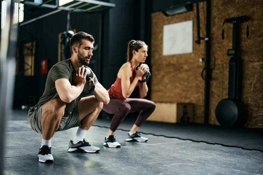 Goblet squat z kettlem trzymanym za rogi przy klatce, pełny przysiad z wyprostowanymi plecami