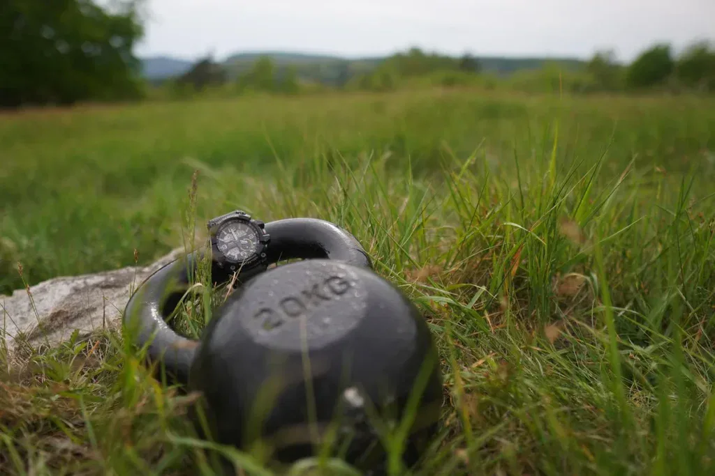 Kettlebell 20 kg na trawie: uchwyt leży poza środkiem masy, inaczej niż w hantli